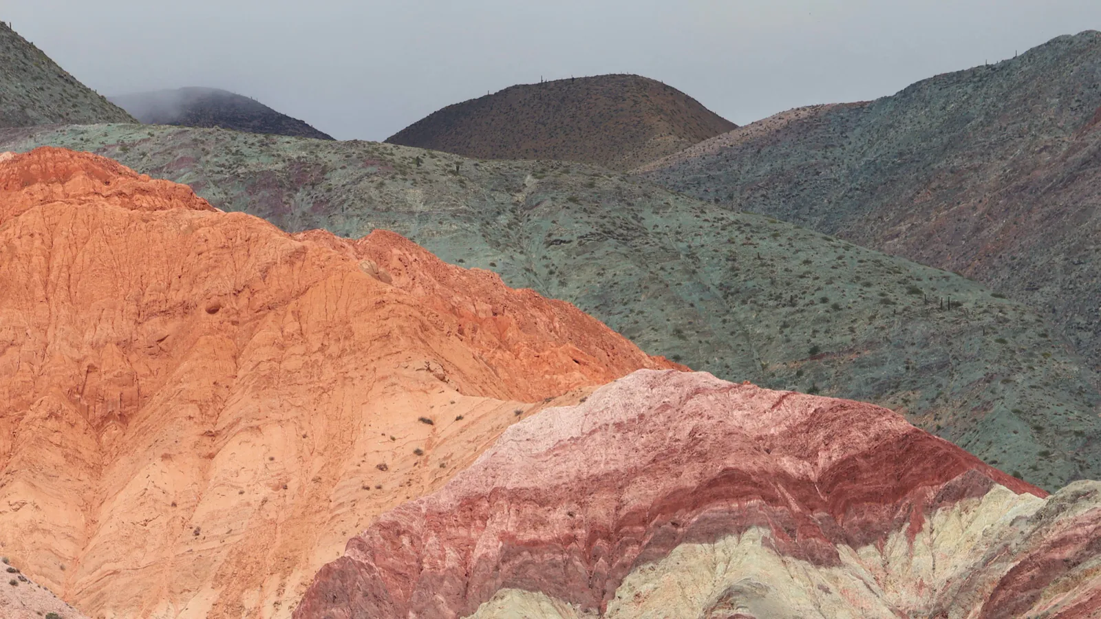 Hills banded in orange, red and pale green rock under a grey sky