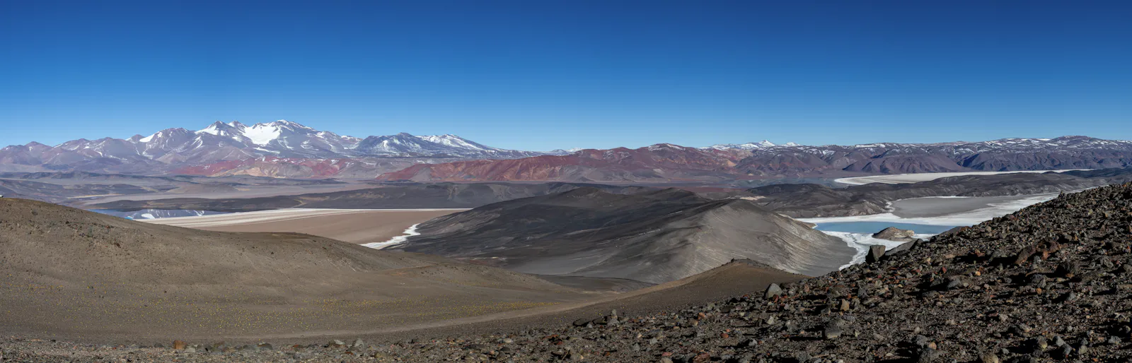 High desert plateau with dark volcanic slopes, salt flats and snow-capped peaks