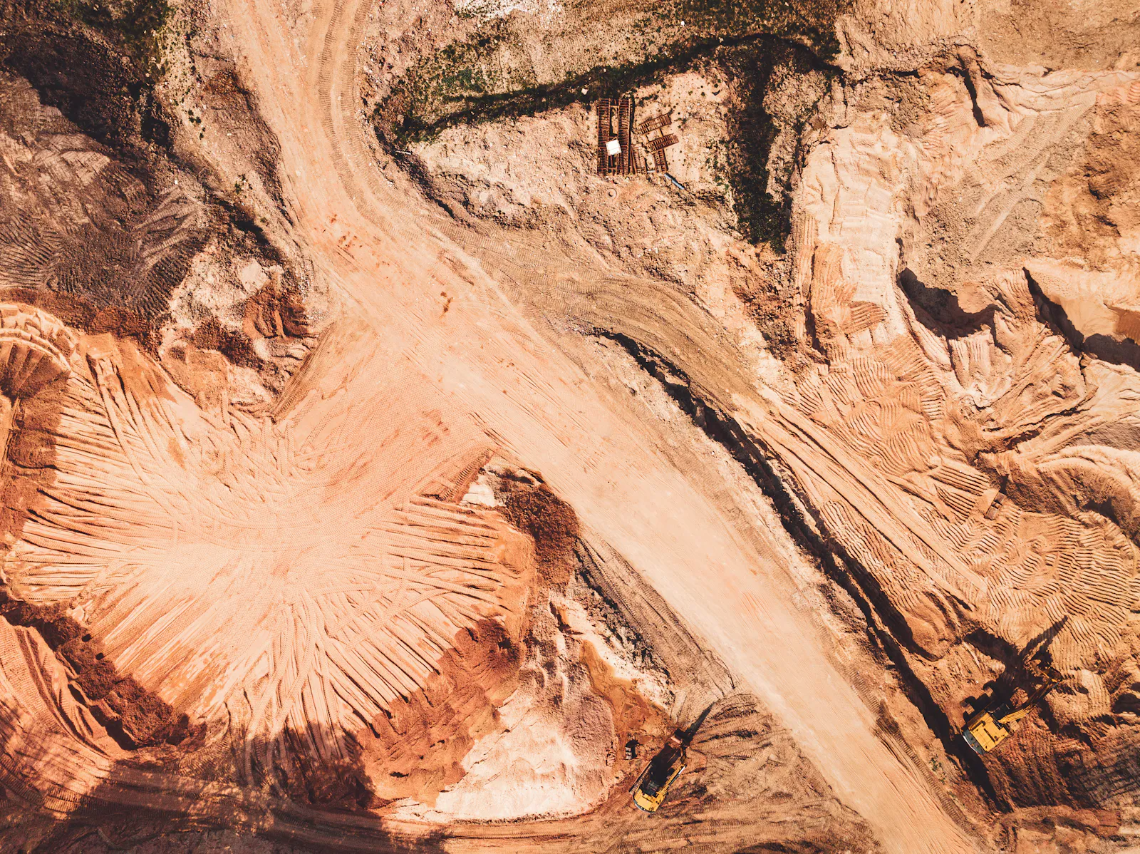 Red-orange cut faces and haul roads of a mine seen from directly above